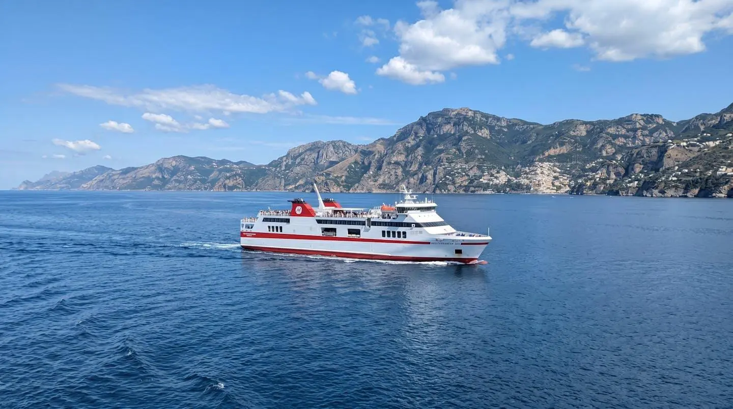 Ferry moderne blanc et rouge naviguant sur une mer Méditerranée calme et bleue avec la côte montagneuse visible à l'horizon